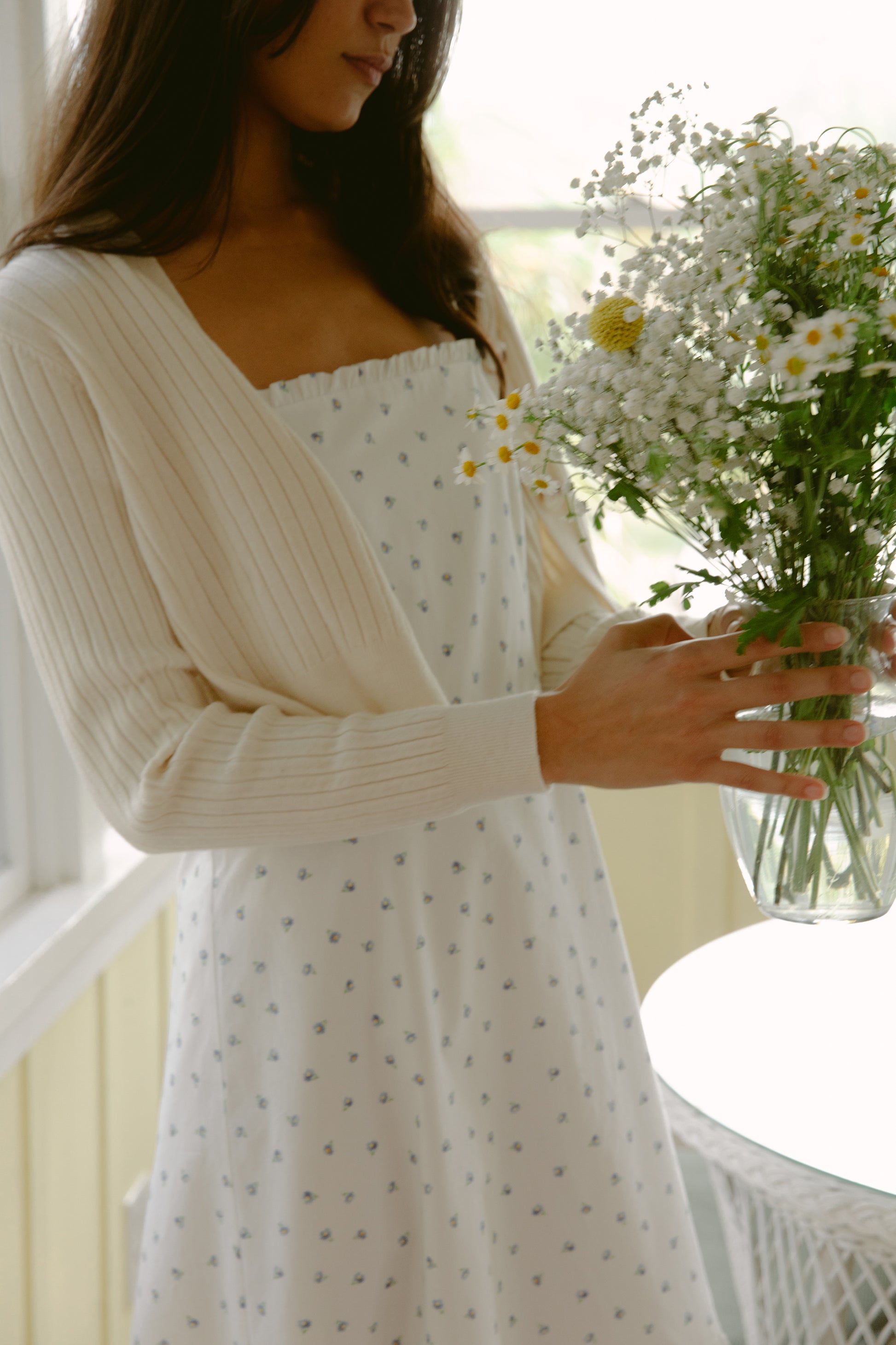 Woman carrying flowers in a white dress and cardigan